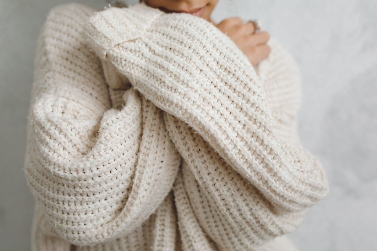 Person in a white knit sweater with long sleeves